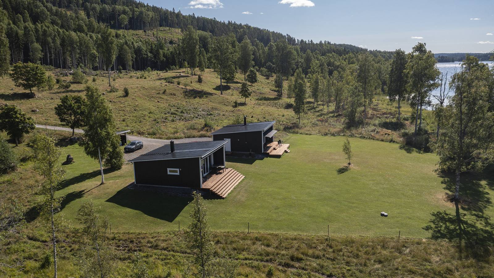 De två stugorna på gräsplanen vid Borgsjön, med skogen och sjön i bakgrunden
