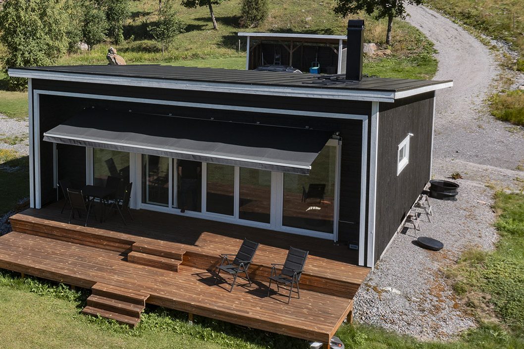 Ängåsen 3 - stuga med mörk träfasad, utfällbar markis och trädäck i flera nivåer